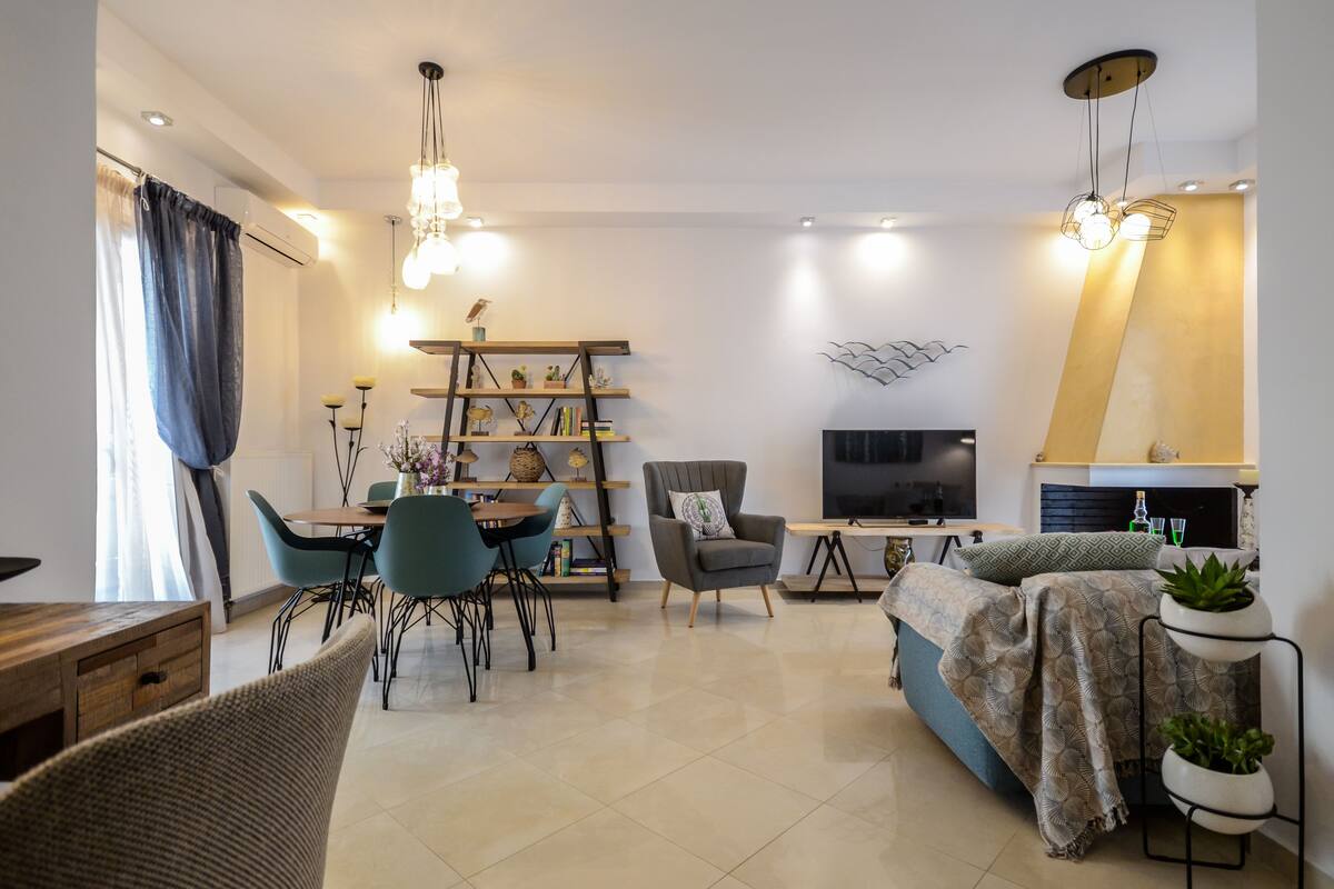 Un salon moderne comprenant un canapé, des fauteuils, une table basse et un téléviseur. On y trouve une bibliothèque avec des objets décoratifs et une petite table sur laquelle est posé un vase.