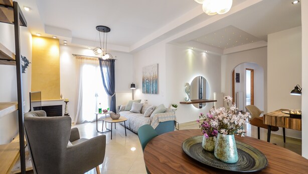 A modern living room with a sofa, chairs, a dining table with a vase of flowers, and a fireplace. - My Island Home (Naxos)