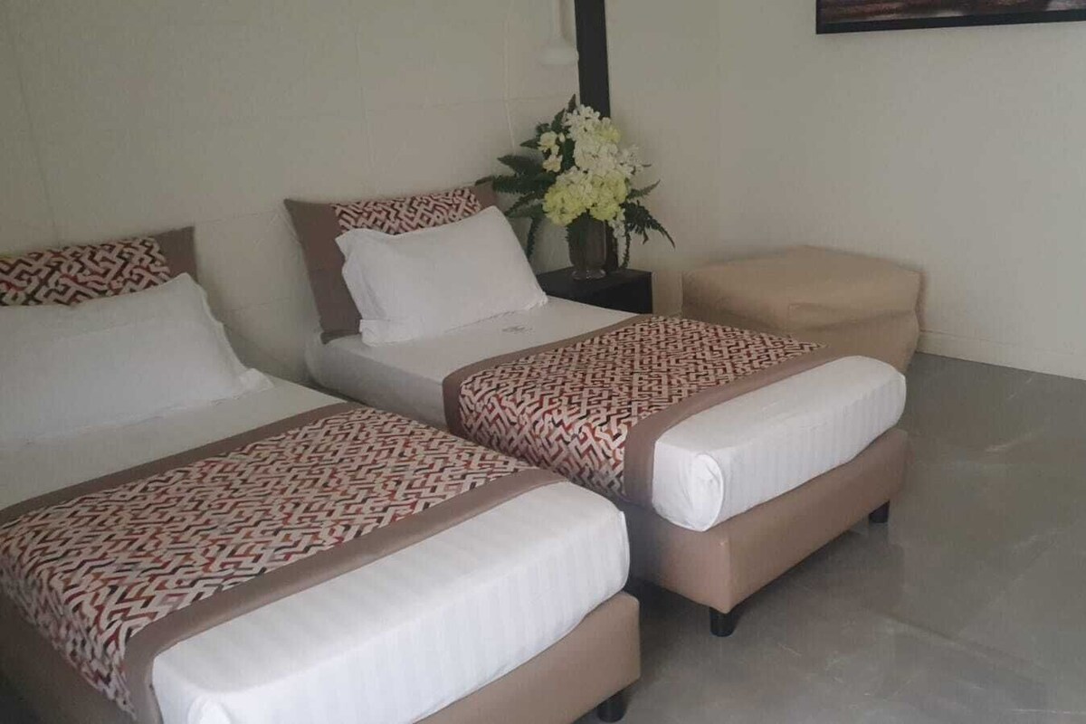 A hotel room with three beds, a small sofa, and a vase of flowers.