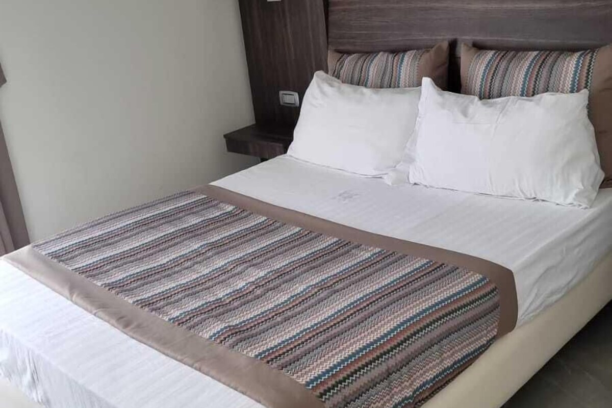A modern hotel room with a large bed, a wooden headboard, and a striped area rug.
