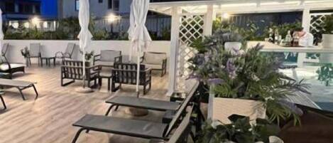 A rooftop terrace with lounge chairs, umbrellas, and a bar area.