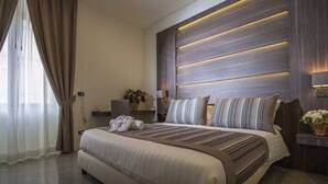A modern hotel room with a large bed, a bedside table, a nightstand, and a wall-mounted lamp. - Palazzo Firenze (Naples)
