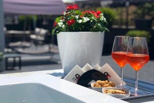 Een tafel met een witte dienblad, twee glazen rode drank, een klein schaaltje met snacks en een potplant met rode bloemen.