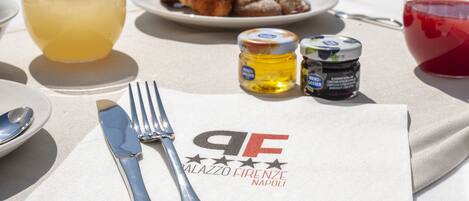 A table with a napkin, fork, knife, two glasses, a plate with croissants, and two jars of jam.