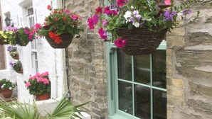 A stone building with hanging flower baskets and a window with a green frame. - Bambu Cottage (Newquay)