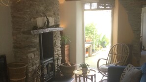 A cozy living room with a stone fireplace, a blue sofa, and a wicker chair. - Bambu Cottage (Newquay)