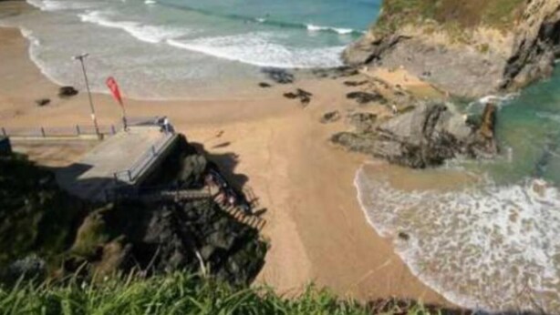 A coastal beach with a rocky shoreline, a sandy beach area, and a small pier. - Bambu Cottage (Newquay)