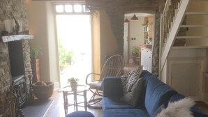 A cozy living room with a blue sofa, a small round table, and a wicker chair. There is a staircase leading to an upper level. - Bambu Cottage (Newquay)
