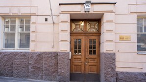 A building entrance with a wooden double door, a sign above the door, and a window with blinds. - Roost Kristianinkatu (Helsinki)