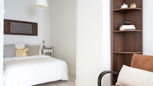 A bedroom with a bed, a nightstand, a chair, and a wooden shelf with decorative items. - Roost Kristianinkatu (Helsinki)