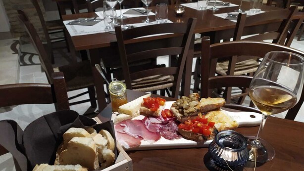 Une table à manger avec une planche de charcuterie, un verre de vin blanc et une bougie.