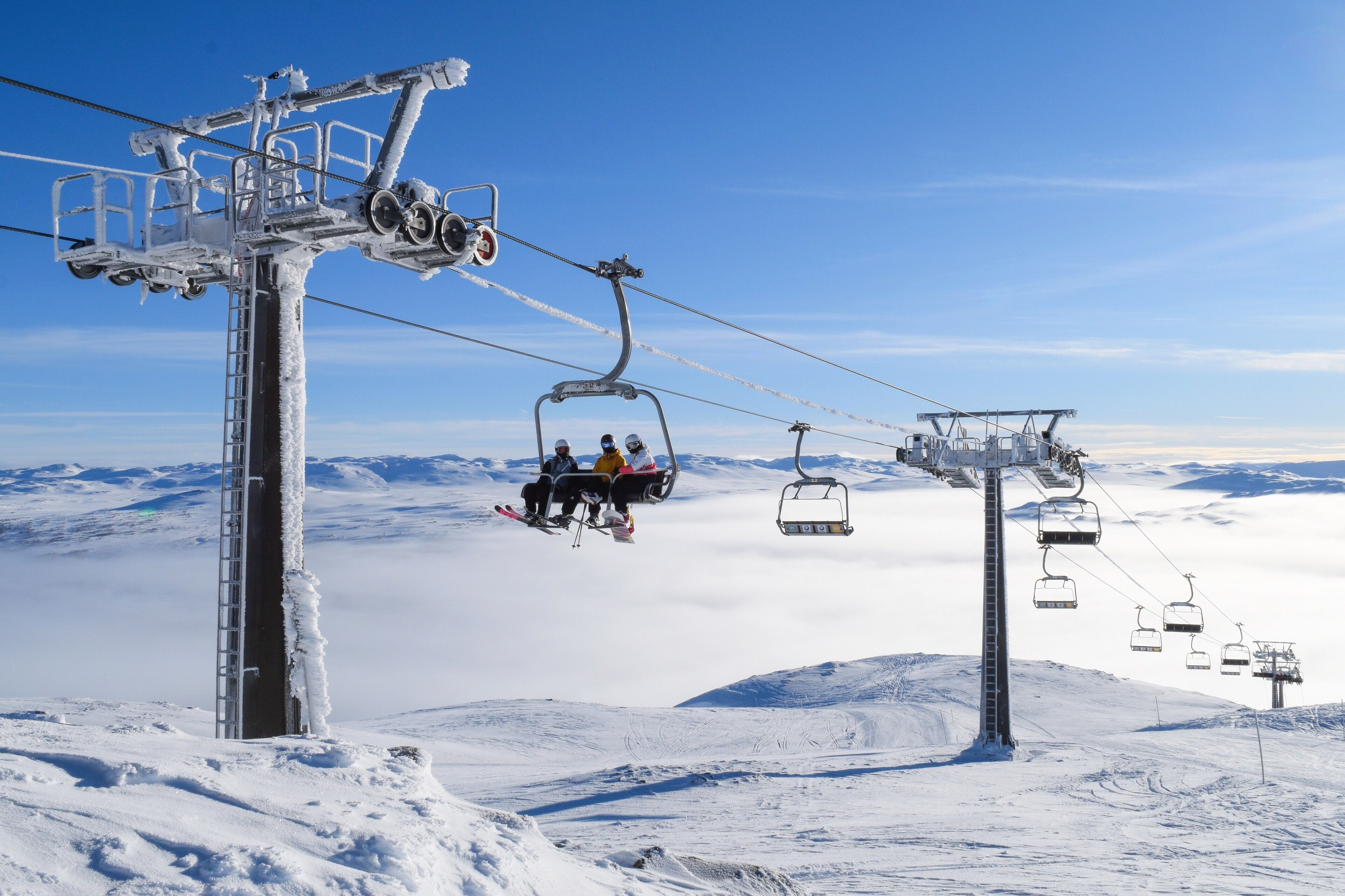 Una seggiovia con passeggeri, un paesaggio montano innevato e cielo sereno.