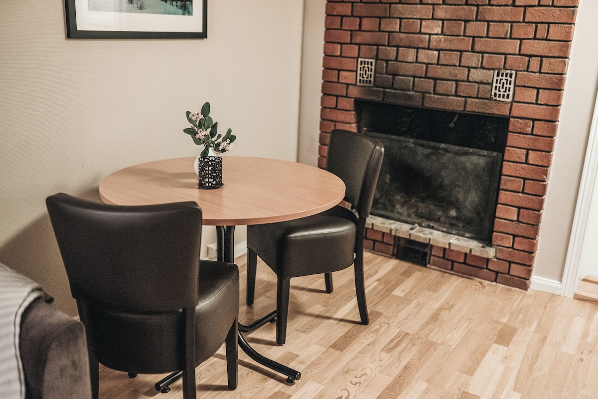 A dining area with a round wooden table, two black chairs, and a small potted plant.