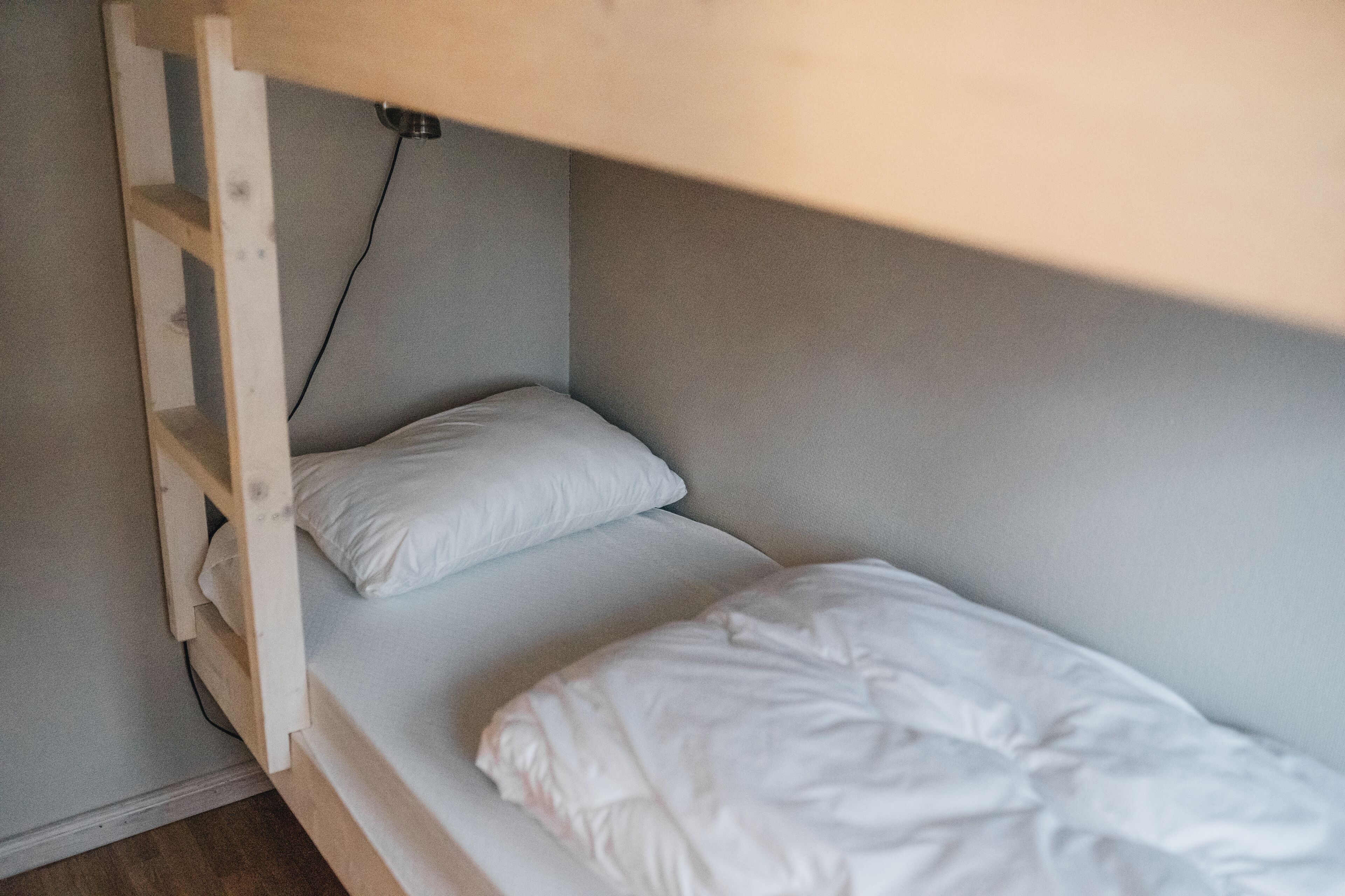 Una cama litera con escalera de madera y un colchón blanco.