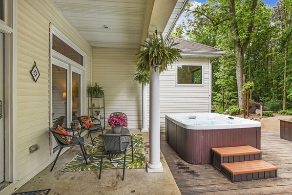 A covered patio with a hot tub, outdoor seating, and a potted plant.