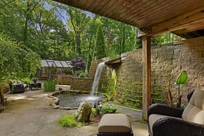A patio with a stone wall, a small waterfall, and outdoor furniture.