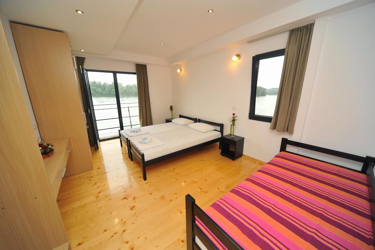 A bedroom with a wooden floor, a bed with a striped blanket, a bedside table with a vase, and a window with curtains.