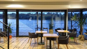 A restaurant with large windows overlooking a lake, wooden flooring, and modern furniture. - B&B Boatel Charlie (Belgrade)