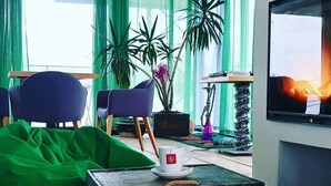 A living room with a green bean bag, a coffee table with a Captain Morgan rum bottle, a TV, and a large plant. - B&B Boatel Charlie (Belgrade)