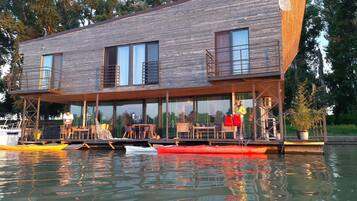 A modern houseboat with a wooden exterior, large windows, and outdoor seating.