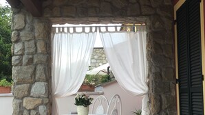 A covered patio area with a stone wall, a white metal table and chair, and a potted plant. - Family room with 4 beds, private bathroom and study with desk.  (Sarzana)
