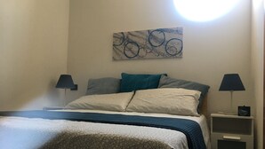 A neatly made bed with patterned bedding, two bedside tables with lamps, and a wall-mounted abstract artwork. - Family room with 4 beds, private bathroom and study with desk.  (Sarzana)