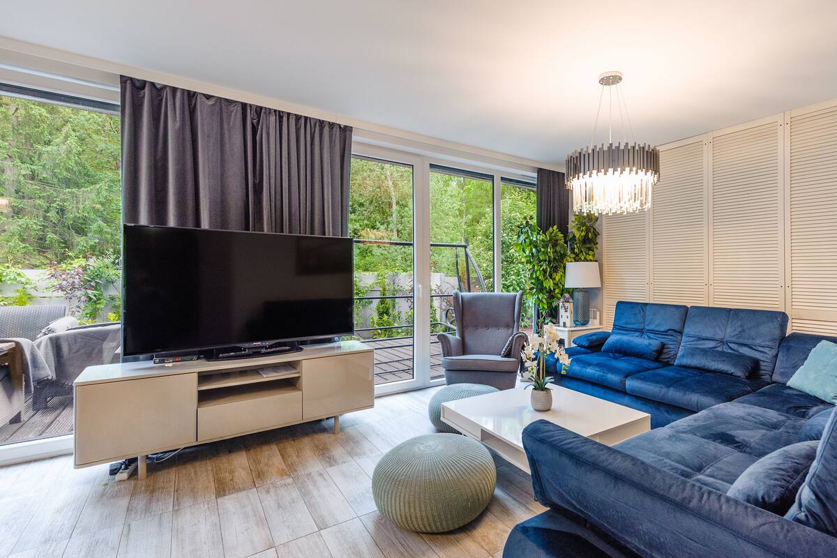 A modern living room with a flat-screen TV, a grey armchair, a blue sofa, and a wooden coffee table.