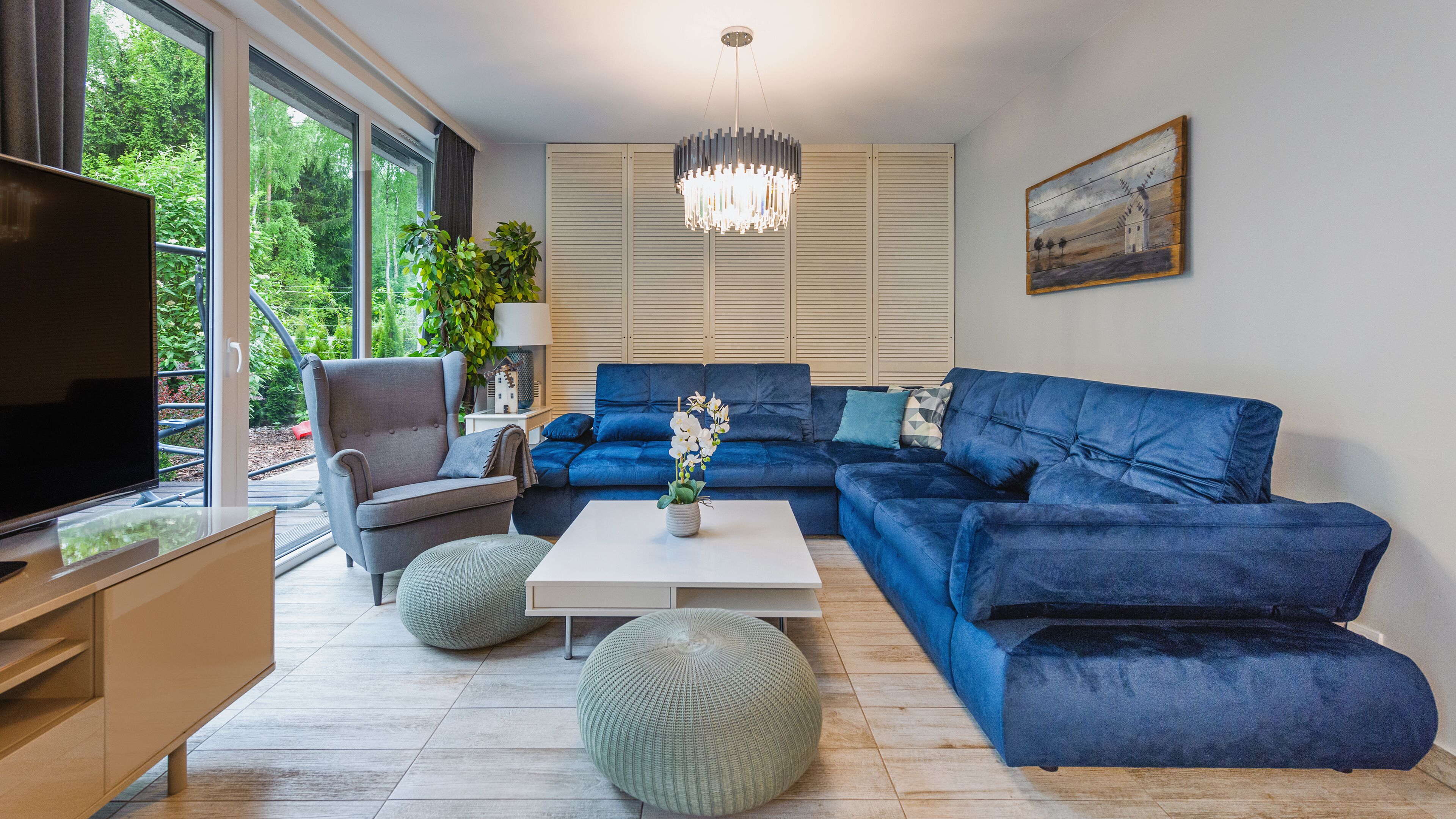 Una sala de estar moderna con un sofá azul, un sillón gris, una mesa de centro blanca y un televisor sobre un mueble de madera.