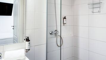 A modern bathroom with a glass shower enclosure, a white tiled wall, a sink with a towel, and a soap dispenser.