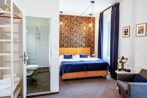 Habitación de hotel con cama, zona de estar, baño con cabina de ducha de vidrio y armario.