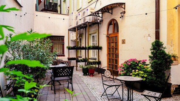 A courtyard with outdoor seating, potted plants, and a building with multiple windows and a door. - BlueBell Hotel (Bratislava)