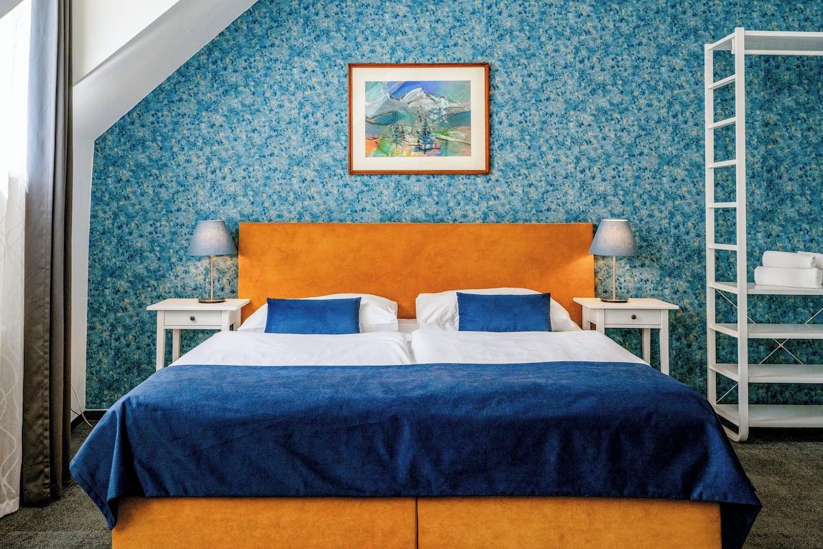 A hotel room with a bed, two nightstands, a framed picture on the wall, and a white shelf unit.