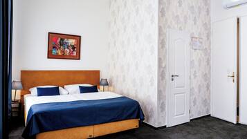 Ein Hotelzimmer mit einem Bett, einem Nachttisch, einer Lampe, einem gerahmten Bild an der Wand und einer Tür mit einem Hinweis.