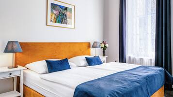 A hotel room with a large bed, two bedside tables, a nightstand, a framed picture on the wall, and a window with curtains.