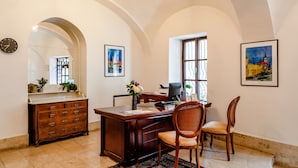 A spacious room with a large desk, two chairs, a dresser, and a large arched window. - BlueBell Hotel (Bratislava)