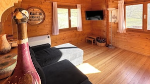 Een gezellig interieur van een chalet met houten wanden en vloeren, een bank, een televisie en een groot raam.