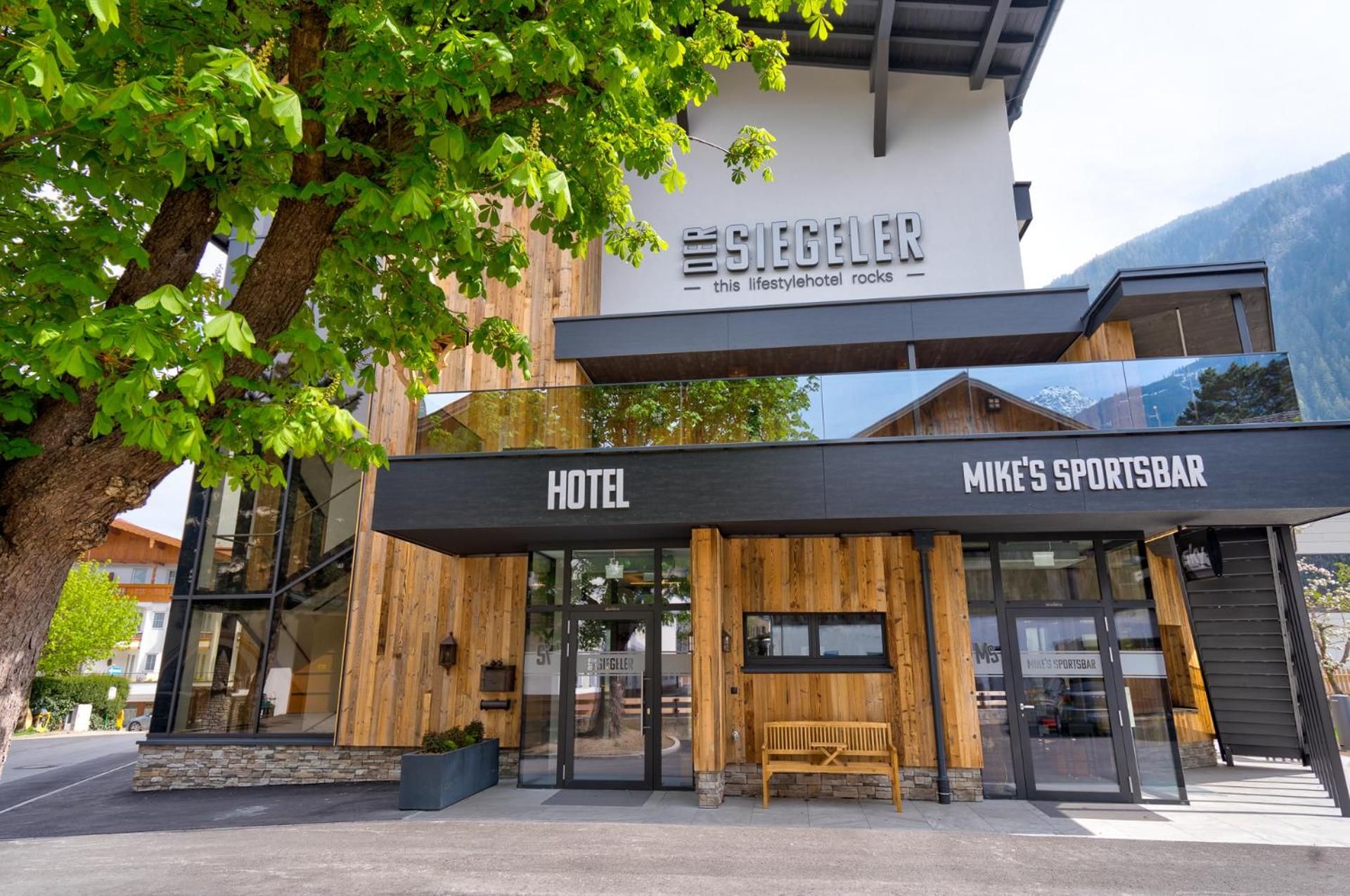 Ein Hotel mit modernem Design, mit einem auffälligen Schild für 'The Siegel' und einer Sportbar namens 'Mike's Sportsbar' darunter.