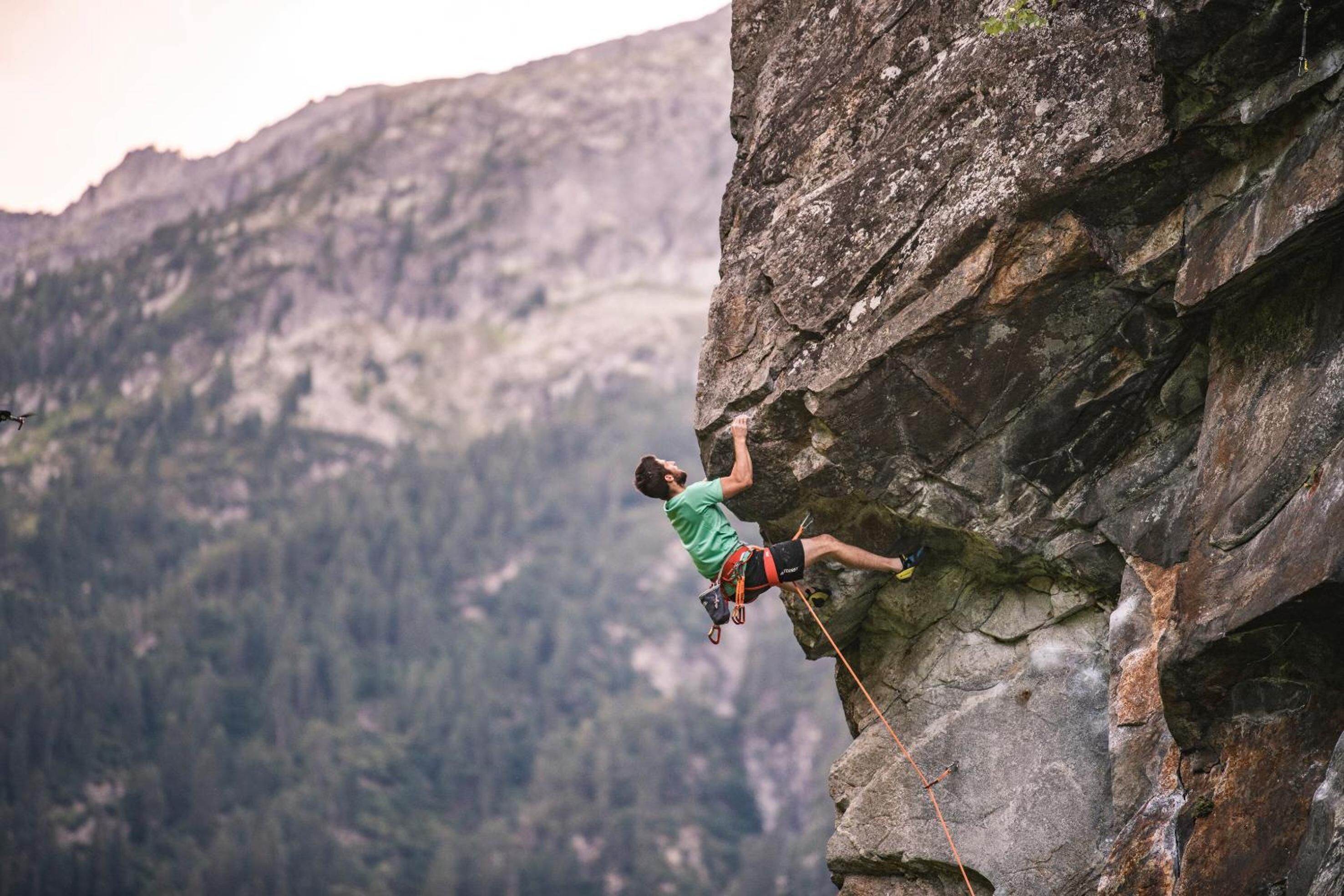 A person rock climbing on a steep cliff with a mountainous background.