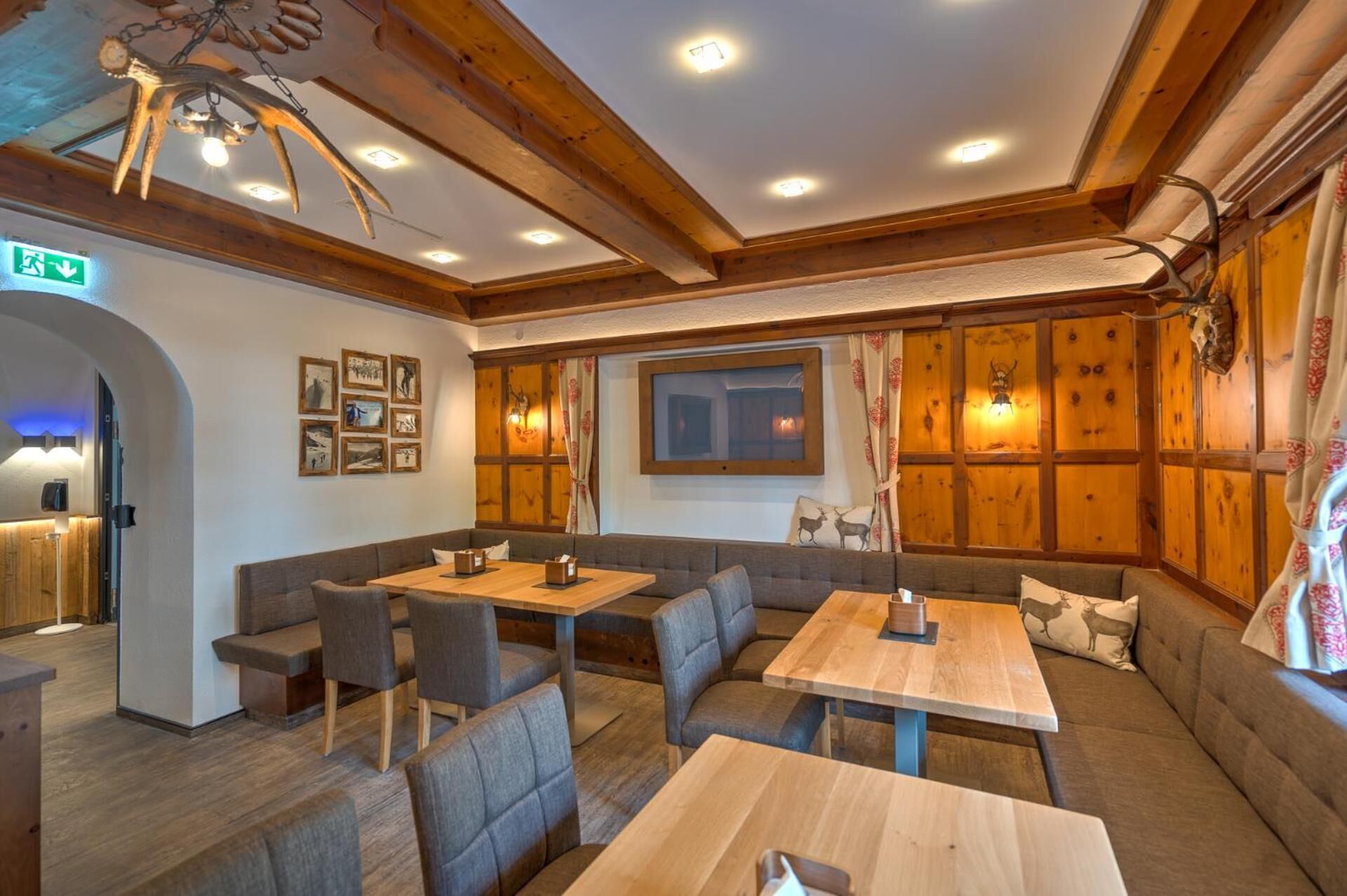 A cozy restaurant with wooden walls, a high ceiling, and a seating area with tables and cushioned benches.