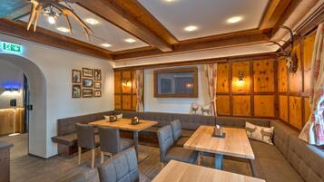 A cozy restaurant with wooden walls, a high ceiling, and a seating area with tables and cushioned benches.
