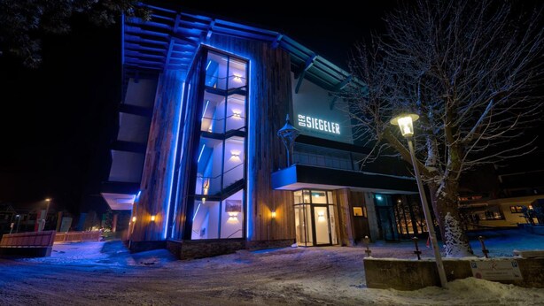 A modern hotel with a prominent entrance, illuminated signage, and a snow-covered ground. - Der Siegeler - this lifestylehotel rocks (Mayrhofen)