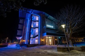 A modern hotel with a prominent entrance, illuminated signage, and a snow-covered ground. - Der Siegeler - this lifestylehotel rocks (Mayrhofen)