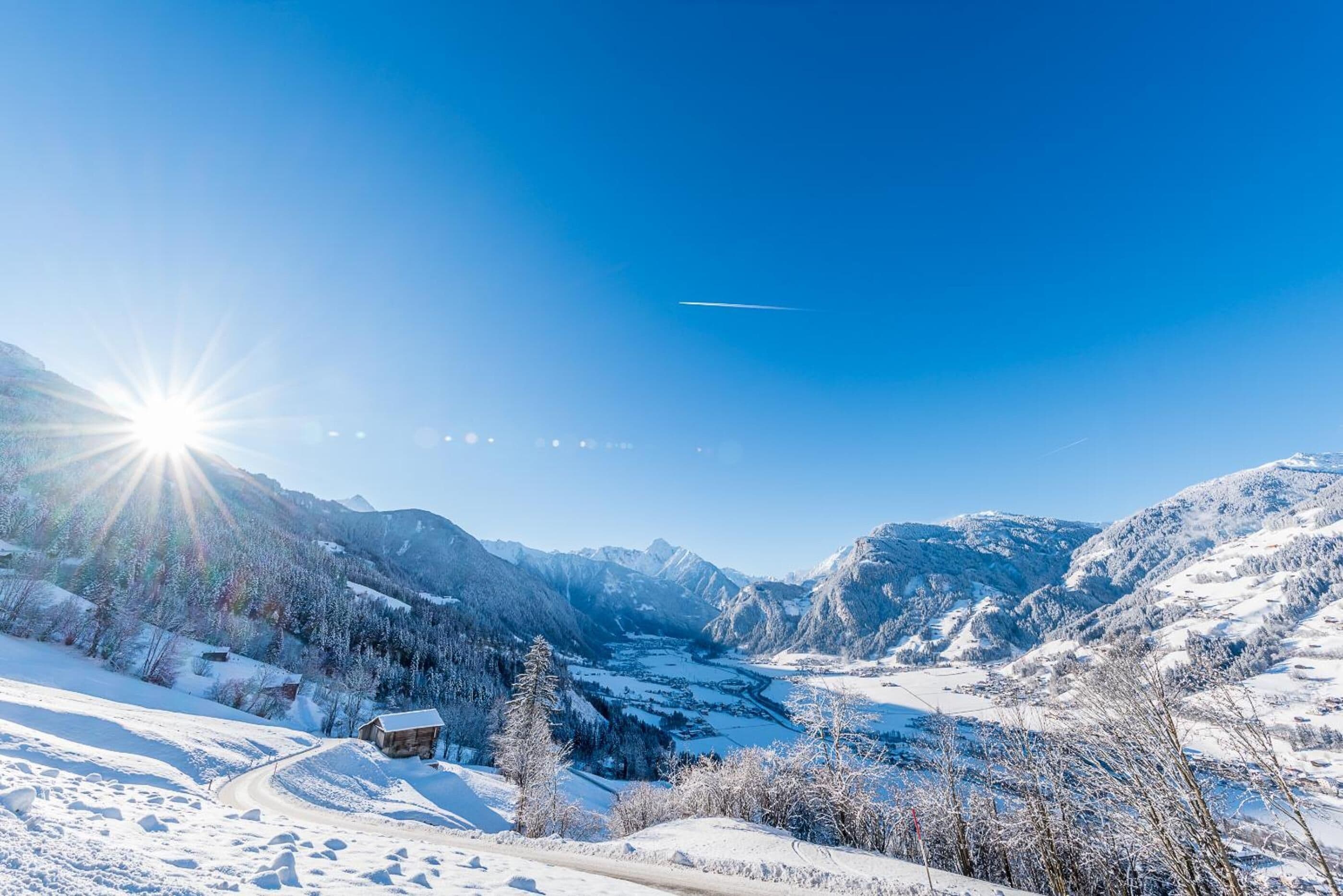 Paisaje montañoso cubierto de nieve, cielo despejado y un sol brillante.