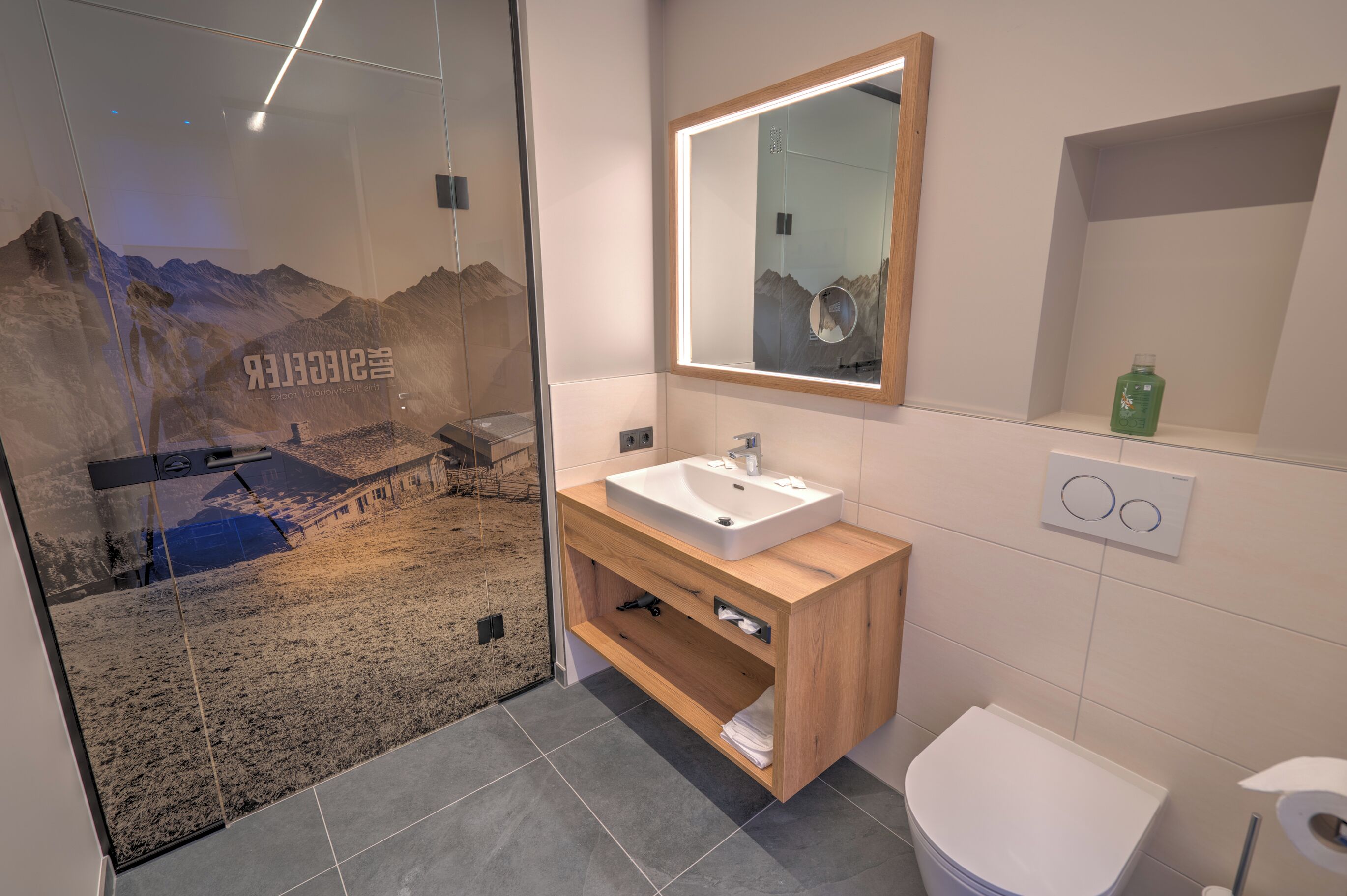 A modern bathroom with a glass shower enclosure, a wooden vanity, a white sink, and a mirror.