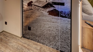 A room with a sliding door featuring a mountain landscape print, a wooden floor, and a bed with pillows. - Der Siegeler - this lifestylehotel rocks (Mayrhofen)
