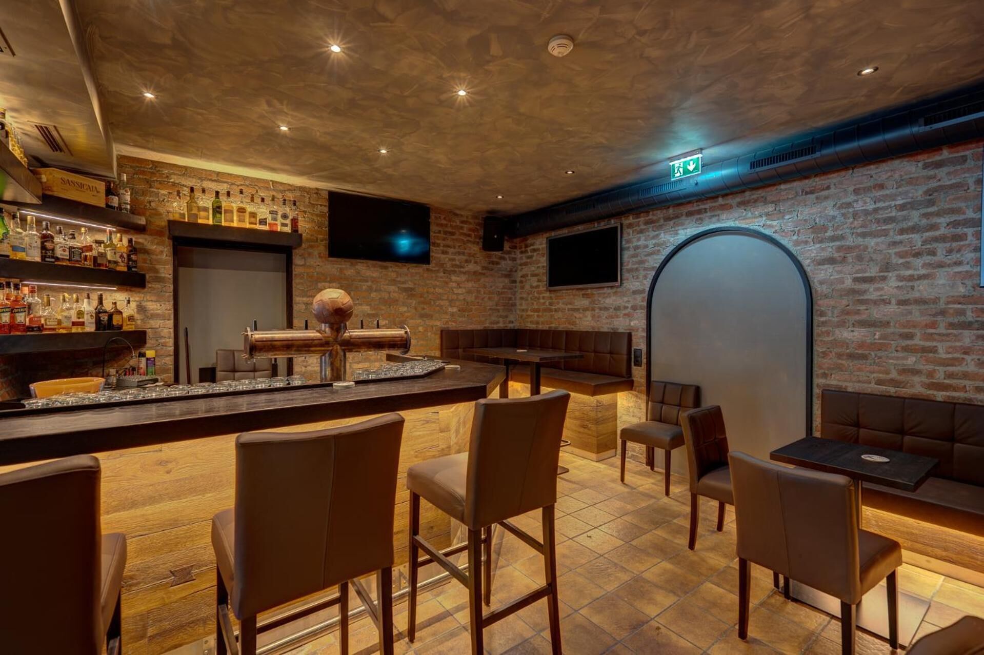 A bar area with a brick wall, wooden bar counter, and seating.