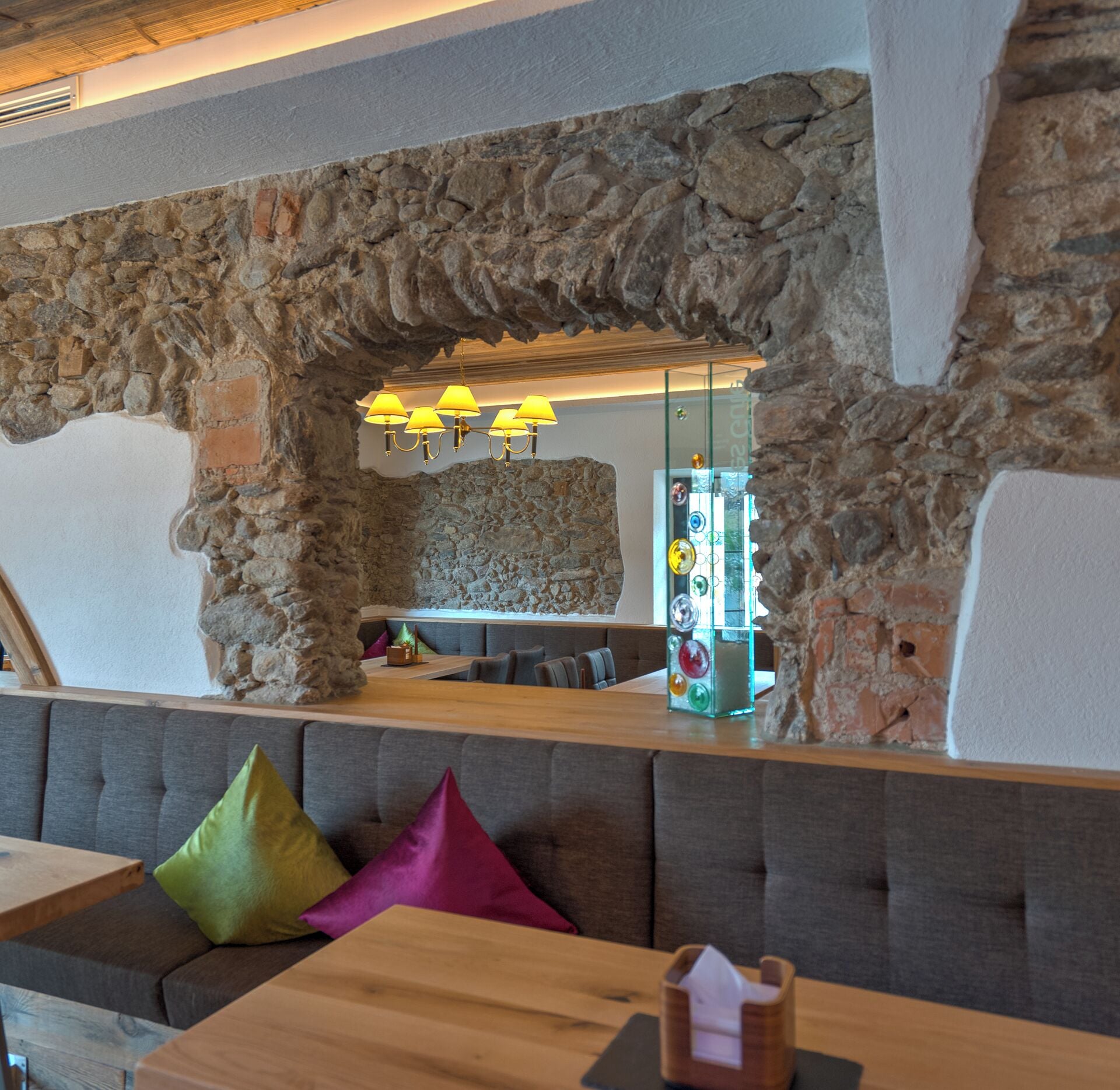 A stone archway leading to a seating area with cushioned benches and a table.