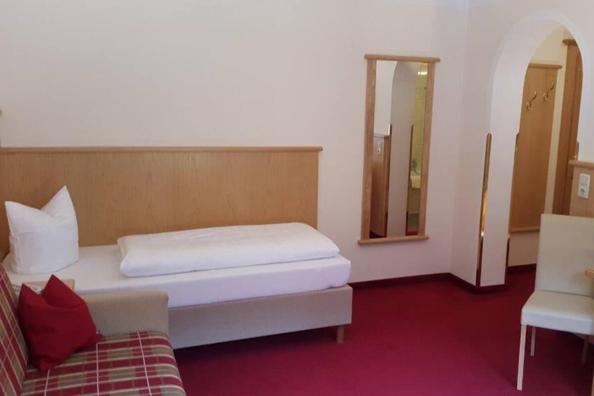 Une chambre d’hôtel avec un lit, un canapé, une chaise, une télévision et un miroir.