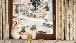 Um banheiro com uma janela grande, cortinas decorativas e um vaso com flores no parapeito.