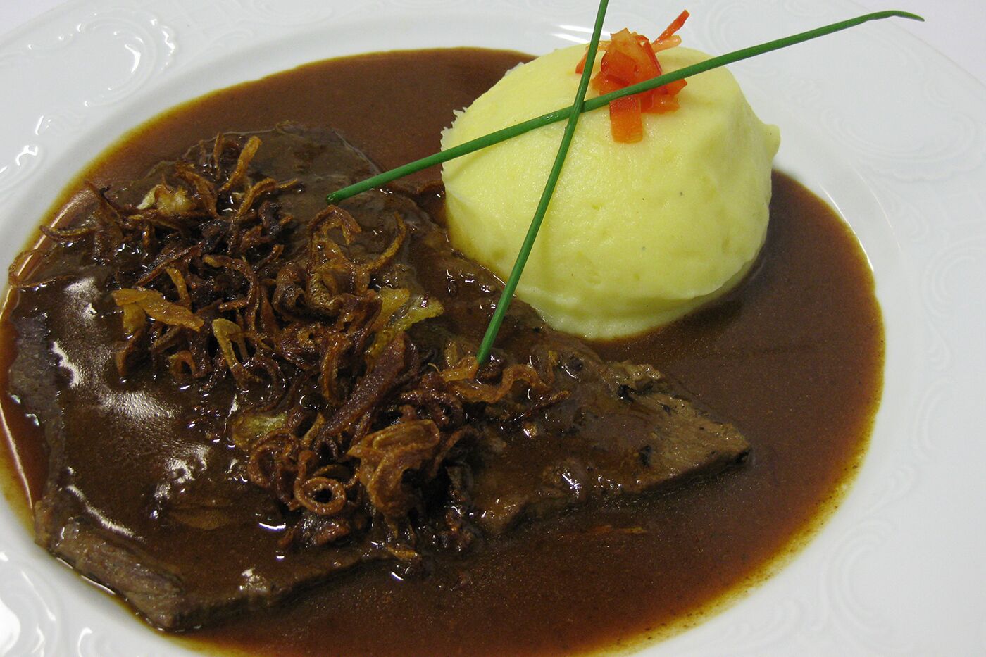 A plate with a meat dish, mashed potatoes, and a garnish.